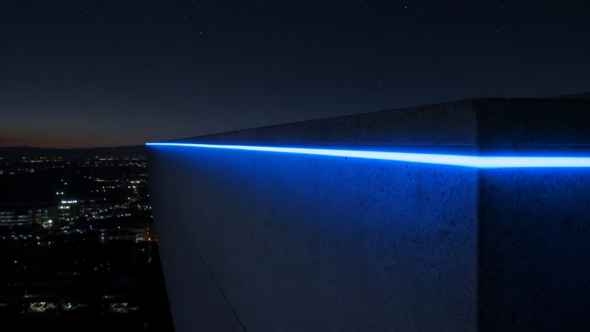 Close-up of a rooftop parapet at night with a continuous glowing side-glow laser fiber optic line in electric blue against a dark sky